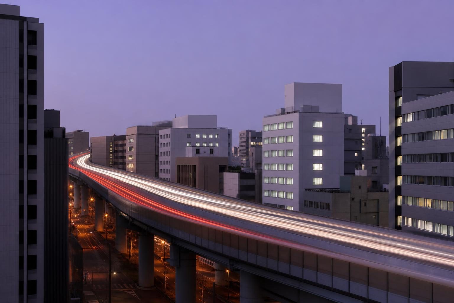 夕方の都市部を走る高架の高速道路と、流れる車のライトの光跡