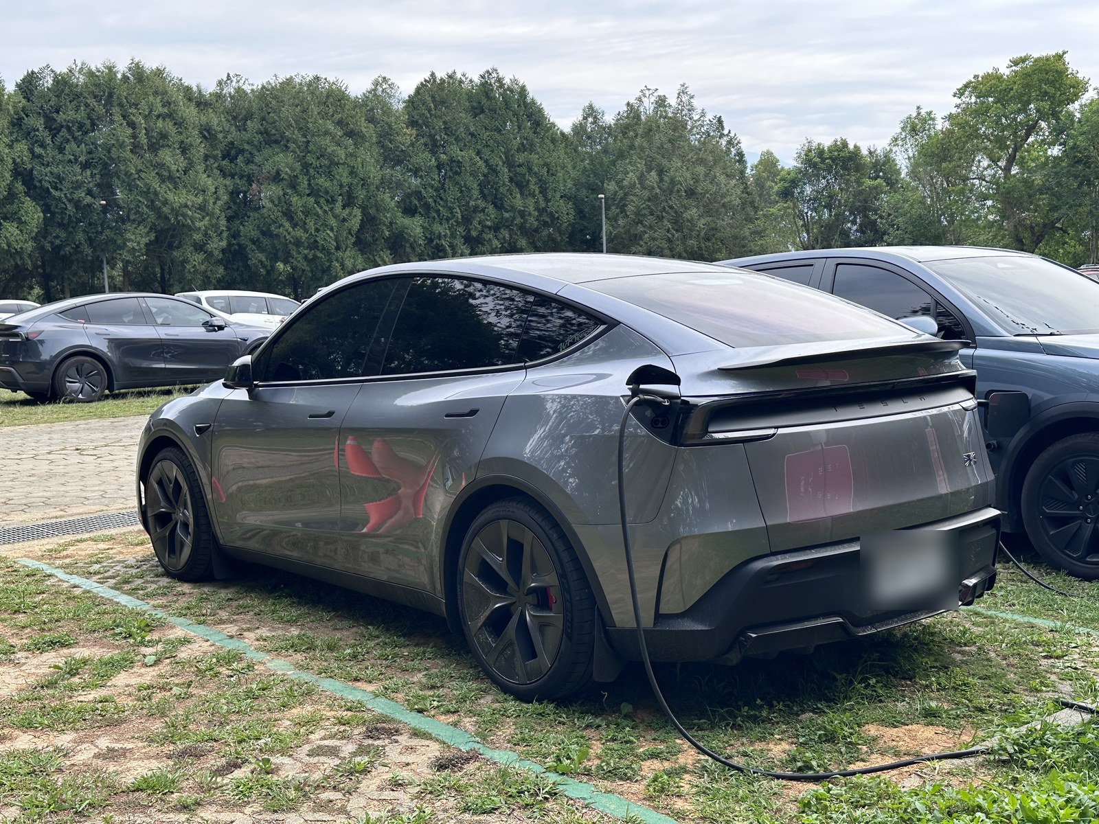 灰色の電気SUVを左後ろから見た写真(駐車場、充電ケーブル接続中)